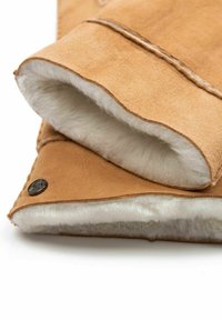 Hellbraune Lederstulpen mit weicher weißer Fütterung. Versehen mit ordentlich gestickten Nähten und einem runden schwarzen Metallakzent auf einer Seite. Weiche Textur sichtbar.