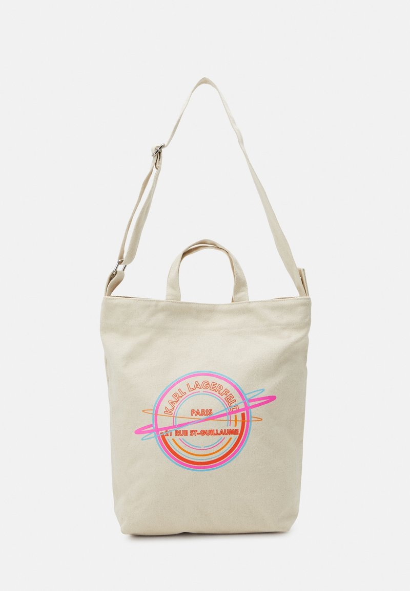 Sac fourre-tout en toile beige avec une poignée supérieure et une bandoulière réglable. Présente un logo imprimé coloré avec texte et motif circulaire.