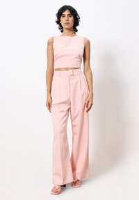 Lichtroze crop top met een ronde hals, gecombineerd met hooggewaist, wijde broek in dezelfde kleur. Glad stof, minimalistisch design.