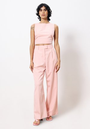 Helles rosa, kurzes Oberteil mit rundem Ausschnitt, kombiniert mit hochTaillierten, weit geschnittenen Hosen in passender Farbe. Glatter Stoff, minimales Design.