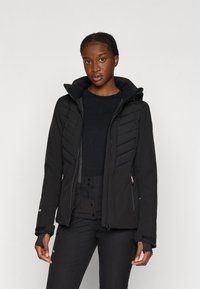 Veste isolée noire avec une fermeture éclair à l'avant, une capuche et une texture matelassée. Elle comprend des poches latérales et des trous pour les pouces dans les poignets.