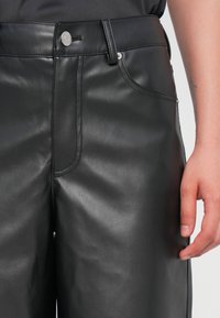 Pantalons en cuir noir avec une texture lisse, dotés d'une taille, de poches avant et de quincaillerie à boutons argentés. Coupe ajustée et design épuré.
