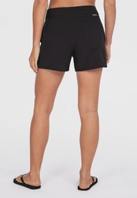 Svarte shorts med glatt tekstur, elastisk midje og en lomme bak. Har et enkelt design uten synlige mønstre eller detaljer.
