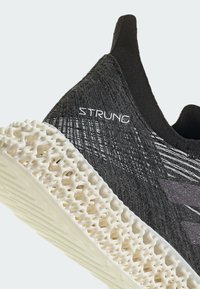 Black athletic shoe with a textured upper, featuring a white, lattice-patterned sole. "STRUNG" branding on the side.