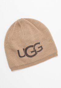 Brun strikket beanie med en ribbet kant, der har et stort sort "UGG" logo på fronten. Blød tekstur og sømløst topdesign.