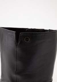 Svart läderstövel med en slät textur, med en rundad skärning upptill och en metallackcent vid öppningen.