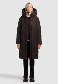 Melnās pūkainās virsjakas ar lielu kapuci, izliekto rakstu, pilna garuma priekšējo rāvējslēdzēju un sānu kabatām. Valkāta virs tumšiem biksēm un zābakiem.