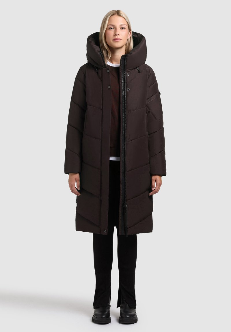 Melnās pūkainās virsjakas ar lielu kapuci, izliekto rakstu, pilna garuma priekšējo rāvējslēdzēju un sānu kabatām. Valkāta virs tumšiem biksēm un zābakiem.