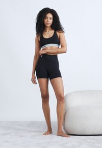 Brassière de sport noire avec une bande rayée gris et blanc, associée à un short noir taille haute. Tissu lisse avec un design minimaliste.