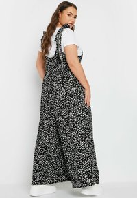 Svart blommig jumpsuit med vita blommor, vida ben och knytband; lager på en vit t-shirt, tillsammans med vita sneakers.