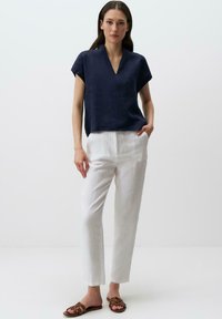 Top in misto di lino blu navy con scollo a V e maniche corte, abbinato a pantaloni bianchi in lino e sandali marroni con cinturini. Tessuto morbido e vestibilità rilassata.