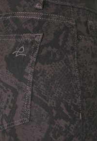 Vaqueros de mezclilla oscura con un patrón texturizado en negro y gris, con costuras visibles, un bolsillo trasero y un detalle de logo bordado.