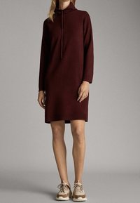 Viininpunainen hupparimekko, jossa on pitkät hihat, polven ylle ulottuva pituus, valmistettu pehmeästä materiaalista, yhdistetty beigeihin lenkkareihin, joissa on korostuksia ja nauhoja.