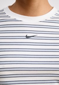 Juostos medvilninis marškinėliai su baltais ir pilkais dryžiais, su juodu Nike logotipu ant krūtinės ir balta banguota apykakle.