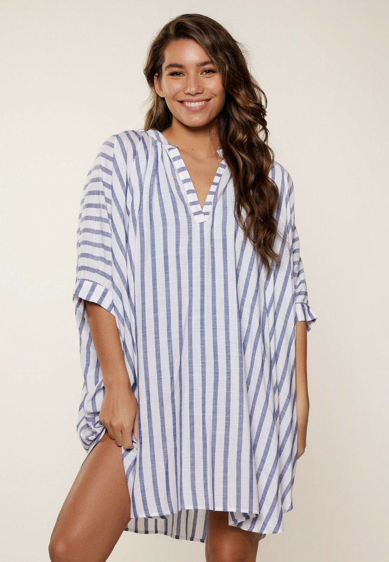 Top kaftano a righe in azzurro chiaro e bianco, realizzato in tessuto leggero. Presenta un collo a V, maniche ampie e una vestibilità rilassata con spacco laterale.