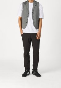 Gilet grigio sopra una t-shirt bianca, abbinato a pantaloni scuri e scarpe nere con strisce bianche. Il gilet presenta un colletto a punta e bottoni.