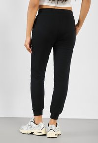 Pantaloni della tuta neri con polsini ed elastico in vita. Abbinati a scarpe sportive bianche e nere. Tessuto morbido, design aderente.