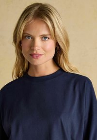 Tumedat t-särgid, millel on ümmargune kaelus ja lühikesed varrukad, on valmistatud pehmest kangast, sisaldades minimaalset õmblust ja sujuvat tekstuuri.