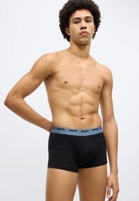 Boxers pretos com cintura elástica azul-claro, com o logótipo 'HUGO' em preto. Textura suave e design ajustado.
