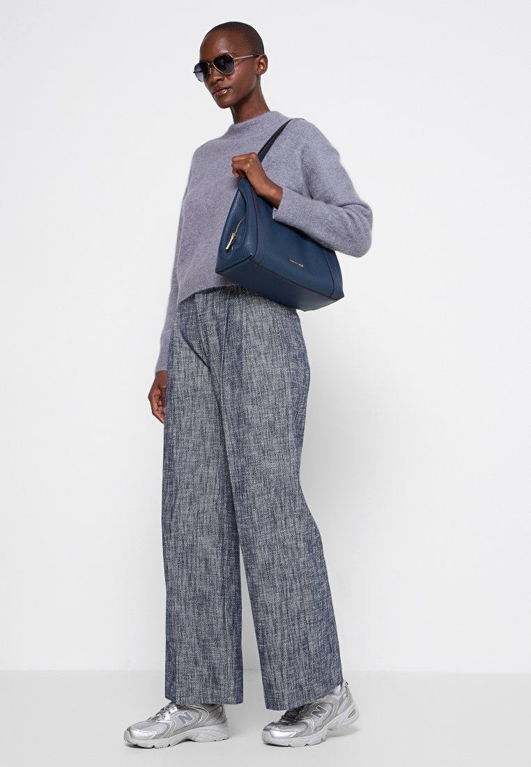 Pull en tricot gris, pantalon bleu large, baskets argentées et un sac marine avec un détail de fermeture éclair dorée. Des lunettes de soleil complètent le look.