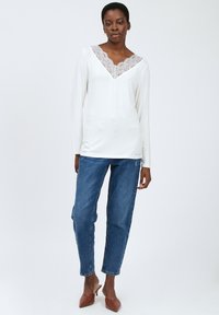 Hvid langærmet top med blonde V-halsdetalje, parret med blå denimjeans og brune hælede mule-sko. Enkel og ren æstetik.