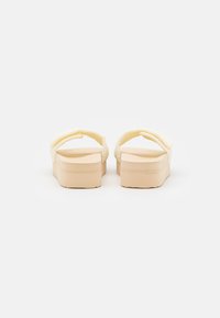 Yellow slip-on sandals with padded straps, a smooth texture, and a thick beige platform sole. Minimalist design with no visible logos.