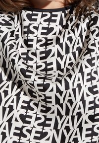 Svart och vitt mönstrat tyg med djärv, upprepad text och grafiska element, samt en slät, satinliknande textur.