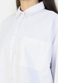 White button-up shirt with a spread collar, featuring a single front pocket and a smooth, lightweight fabric. Relaxed fit.