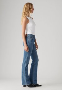 Lättviktig, åtsittande vit linne topp kombinerad med utsvängda blå denim jeans. Jeansen har en klassisk textur med subtila sömmar och en brun läderlapp.