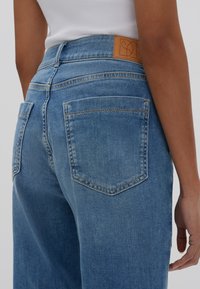 I jeans di denim azzurro chiaro presentano una vita alta, un design a gamba dritta e due tasche posteriori. Una toppa in pelle marrone è visibile in vita.