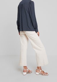 Laivastonsininen polkapilkkuinen pusero, jossa on pönkitetyt hihat, yhdistettynä kermaisiin leveälahkeisiin housuihin ja valkoisiin sandaaleihin, joissa on paksut korot ja remmit.