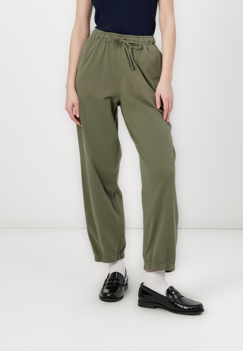 Olivengrønne, elastiske bukser med tapered pasform og opdækkede sømme. Båret med sorte loafers og hvide sokker. Har en afslappet, loose fit.