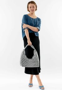 Bolso hobo gris acolchado con un acabado texturizado, asa sobredimensionada y una silueta suave; el modelo lleva una camisa de mezclilla y una falda negra.