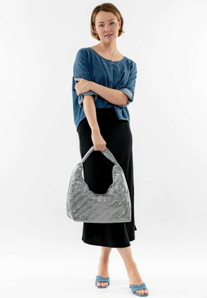 Bolso hobo gris acolchado con un acabado texturizado, asa sobredimensionada y una silueta suave; el modelo lleva una camisa de mezclilla y una falda negra.