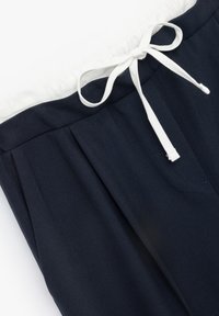 Mørkeblå bukser med hvid elastisk talje og snoretræk. Har frontfolder og en diskret lomme. Glat, letvægtsstof.