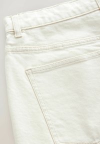 Weißer Denim-Stoff mit glatter Textur. Verfügt über eine Gesäßtasche mit schrägen Nähten und hellbeiger Naht überall.