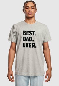 Camiseta de algodón gris con texto negro en negrita que dice "MEJOR. PAPÁ. DE TODOS LOS TIEMPOS." Diseñada con mangas cortas y un cuello redondo.