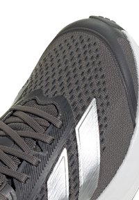 Chaussure de sport grise et noire avec tissu en mesh, lacets épais et deux bandes argentées réfléchissantes sur le côté, montrant la zone des orteils et des lacets.