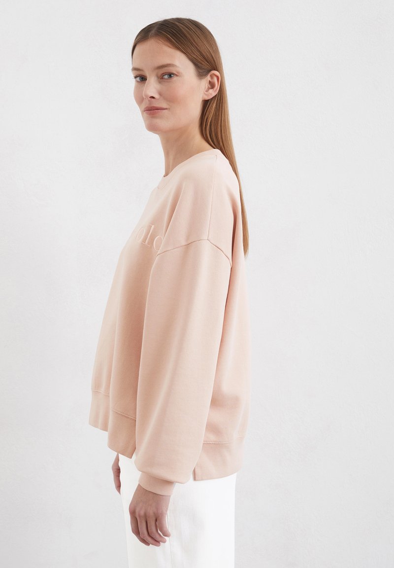 Jasnoróżowy sweatshirt z prążkowanymi mankietami i dołem, w oversize'owym fasonie, z delikatnym wytłoczonym napisem z przodu. Gładki materiał z bawełny.