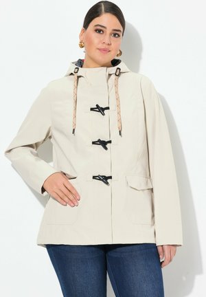Vedenpitävä beige takki hupulla, nyörisulkimilla ja mustilla yksityiskohdilla. Ominaisuuksiin kuuluu kaksi etutaskua ja rento leikkaus. Silkkinen pinta.