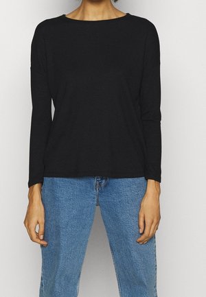 Maglietta nera a maniche lunghe con un ampio scollo, realizzata in tessuto morbido e strutturato. Abbinata a jeans azzurri a gamba dritta.