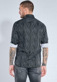 Schwarzes gestreiftes Hemd mit weißen Linien, kurzen Ärmeln und aufgerollten Bündchen; verfügt über einen sauberen Kragen und ein dezentes Strukturmuster.