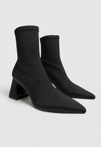 Bottines noires en tissu lisse, avec un bout pointu et un talon carré. Le design comprend des côtés élastiqués et des coutures minimales.