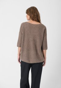 Brun strikket sweater med løs pasform, korte ærmer og vid halsudskæring. Blød tekstur og en let buet kant, parret med sorte bukser.