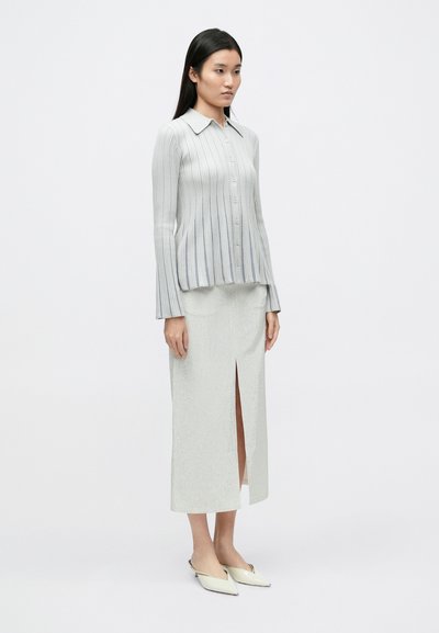 Svetlosivý rebrovaný úpletový dlhý rukáv s golierom, doplnený o zodpovedajúcu sukňu po kolená s rozparkom vpredu. Topánky so špicatou špičkou.