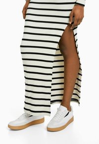 Robe maxi à rayures noires et blanches avec un fente sur le côté, assortie à des baskets blanches avec un accent noir et une semelle en gomme.