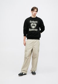 Czarna bluza z nadrukiem "Carhartt University", w połączeniu z beżowymi spodniami cargo. Ubranie uzupełniają czarne trampki z białymi akcentami.