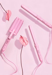 Trzy różowe narzędzia do stylizacji włosów na różowym tle: lokówka, prostownica z trzema cylindrami oraz prostownica do włosów, z teksturowanymi uchwytami i przyciskami.