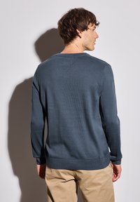 Pull bleu foncé à manches longues, avec un col et des poignets côtelés, texture lisse et ourlet droit, associé à un pantalon beige clair.