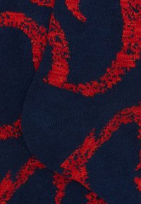 Calzini lavorati a maglia con sfondo blu navy e un audace motivo astratto rosso. La texture è liscia con colori a contrasto e polsini a coste.